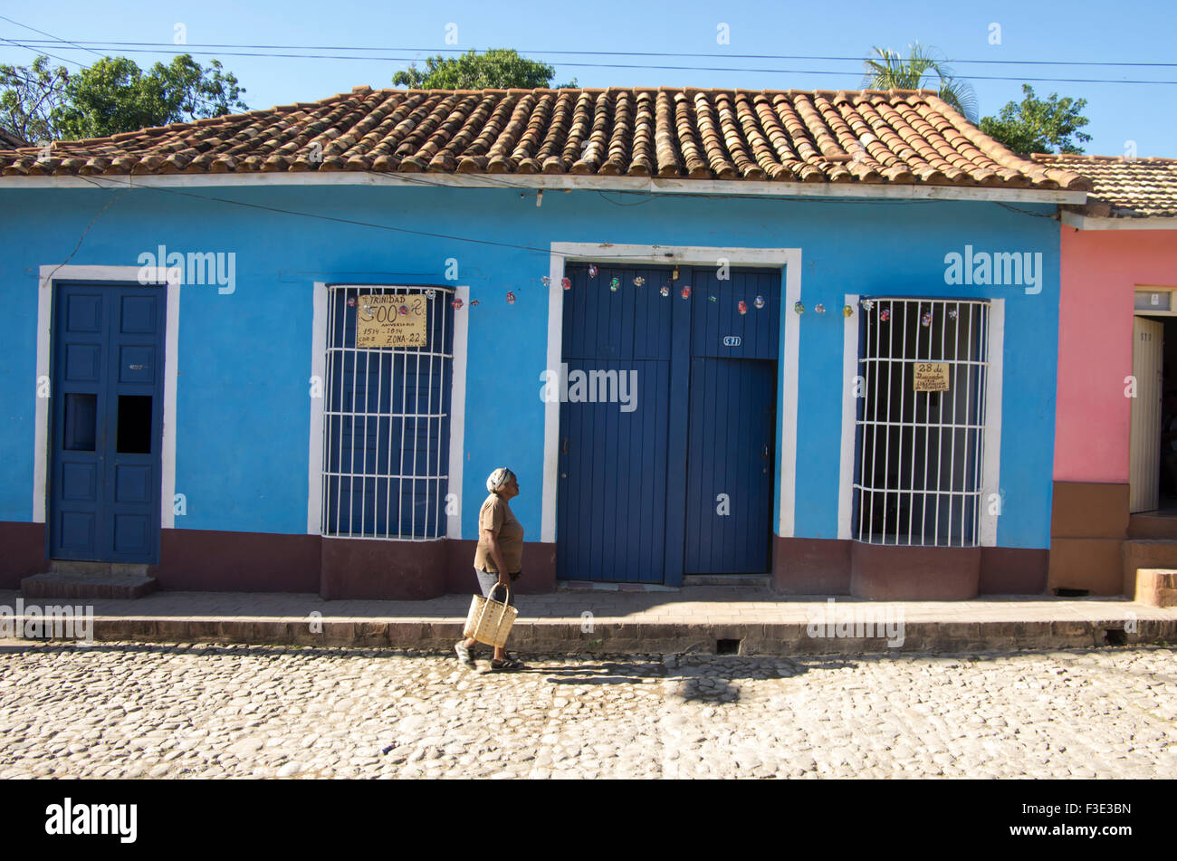 La mujer camina pasado una tradicional casa de estilo colonial español con ventanas con barrotes en Trinidad, provincia de Sancti Spiritus Foto de stock