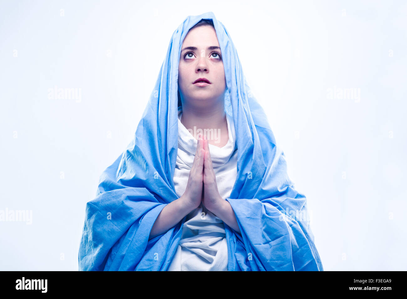 Virgen María rezando con velo azul sobre fondo blanco Fotografía de