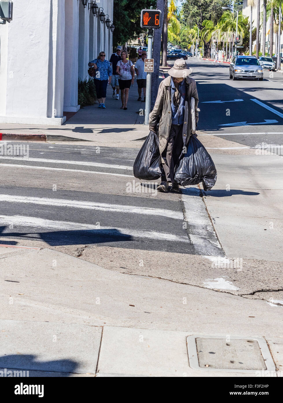 Un adulto mayor sin hogar hombre vestido con un abrigo largo y un sombrero  en un día caluroso y llevar una gran bolsa de basura de plástico negro en  cada hectárea Fotografía