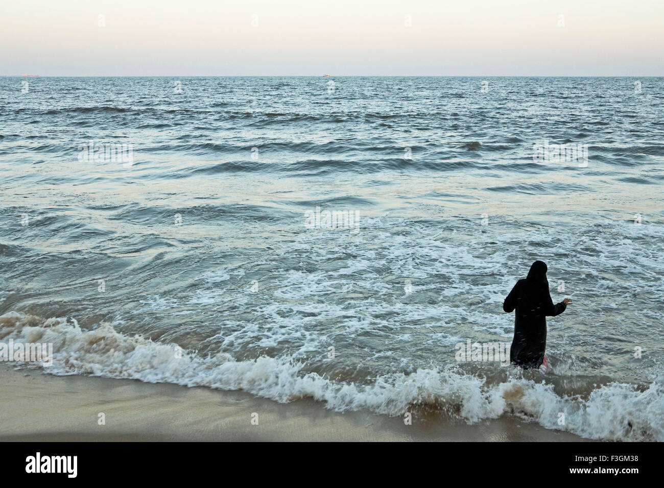 Una niña musulmana llevar un negro burkha disfrutando de las olas, salpicaduras de ella en la Playa Marina ; ; ; Chennai Tamil Nadu, India Foto de stock