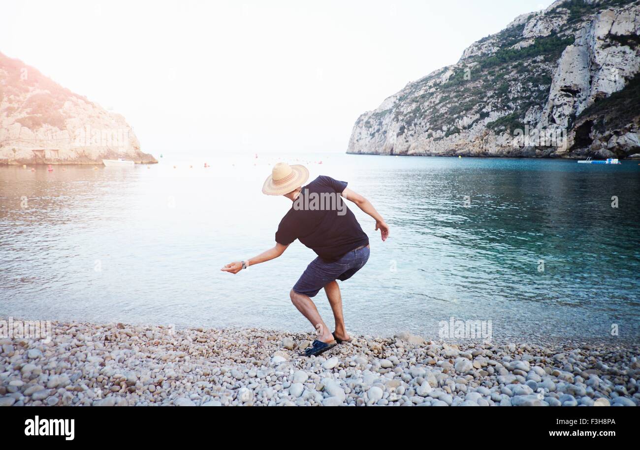 Vista trasera del joven rozando las piedras de la playa, de Jávea, España Foto de stock