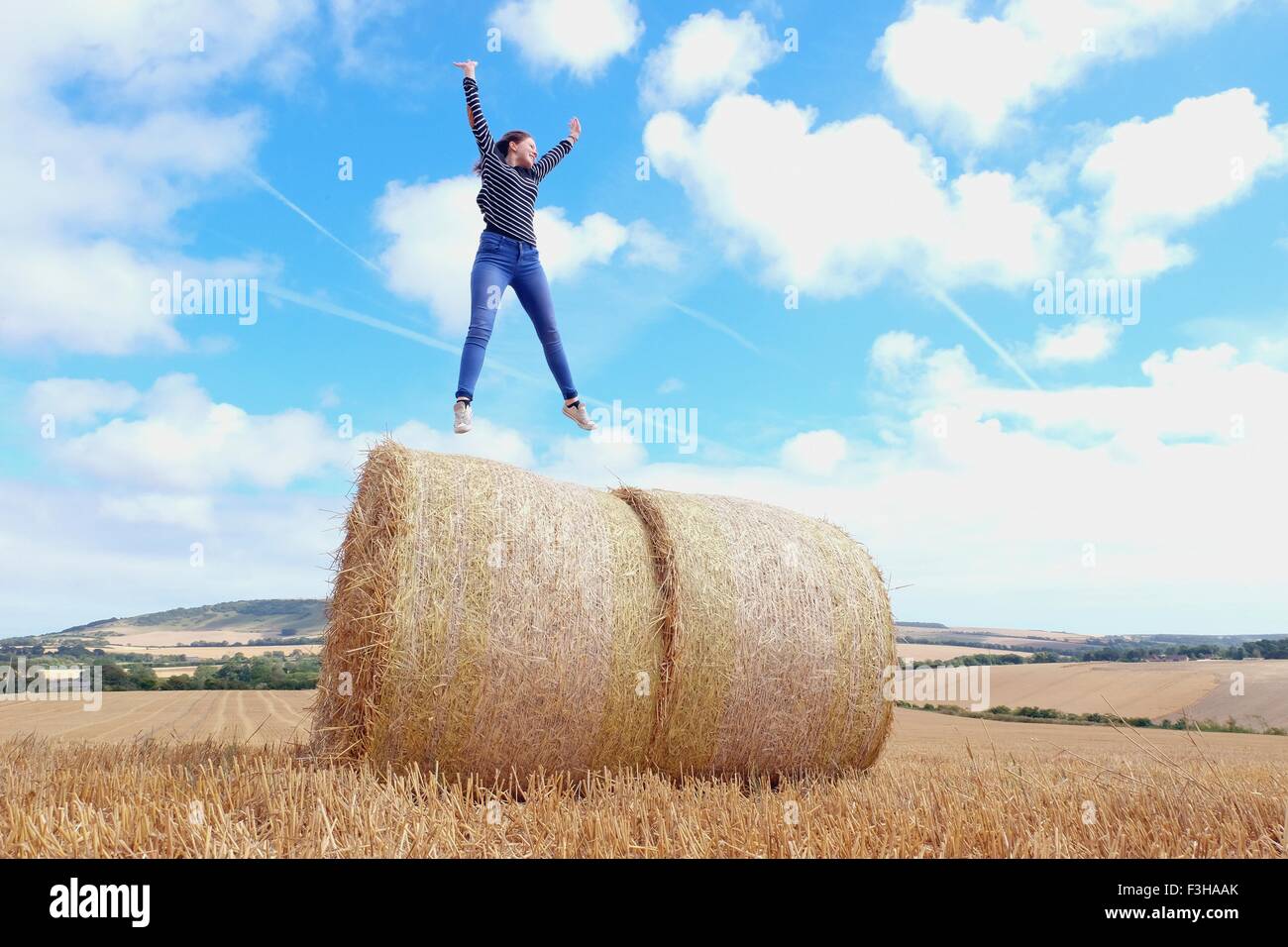 Mujer joven saltando encima de montones de heno en el campo cosechado Foto de stock