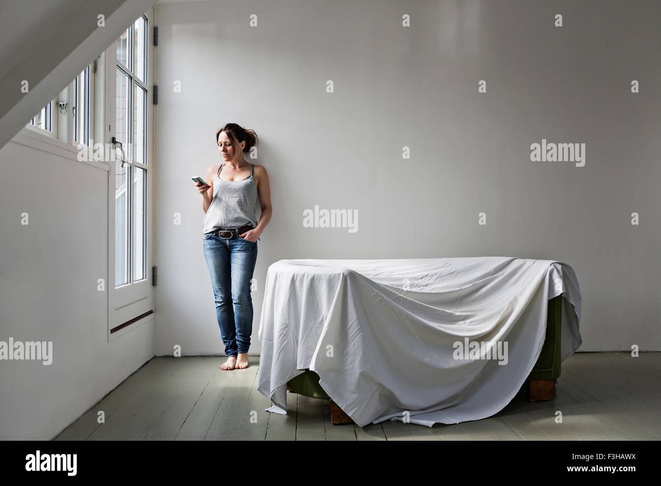 Mujer madura de pie en parte amueblado casa, usando el teléfono móvil Foto de stock