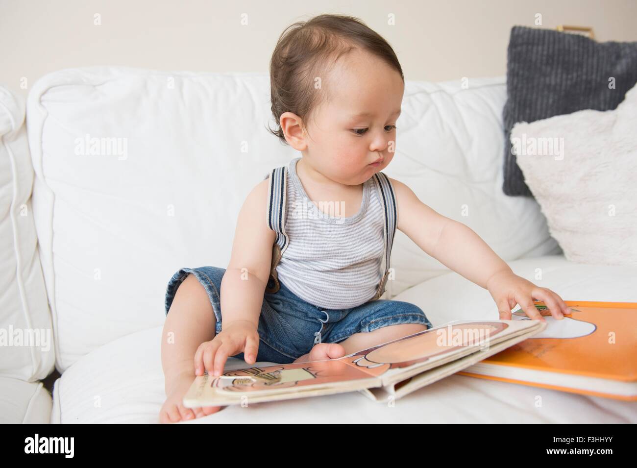 Baby Boy sentado en el sofá viendo libro de imágenes Foto de stock