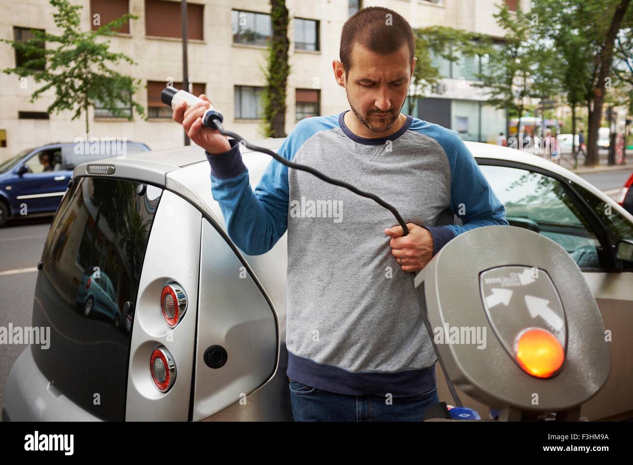 Hombre cargando un coche eléctrico, en la calle París, Francia Foto de stock