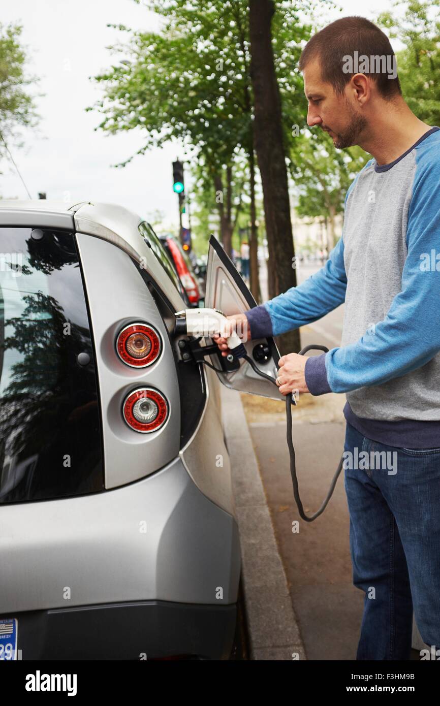 Hombre cargando un coche eléctrico, en la calle París, Francia Foto de stock