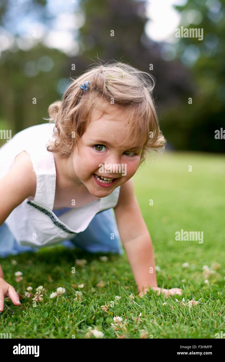 Vista frontal de la niña en las manos y las rodillas mirando a la cámara sonriendo Foto de stock