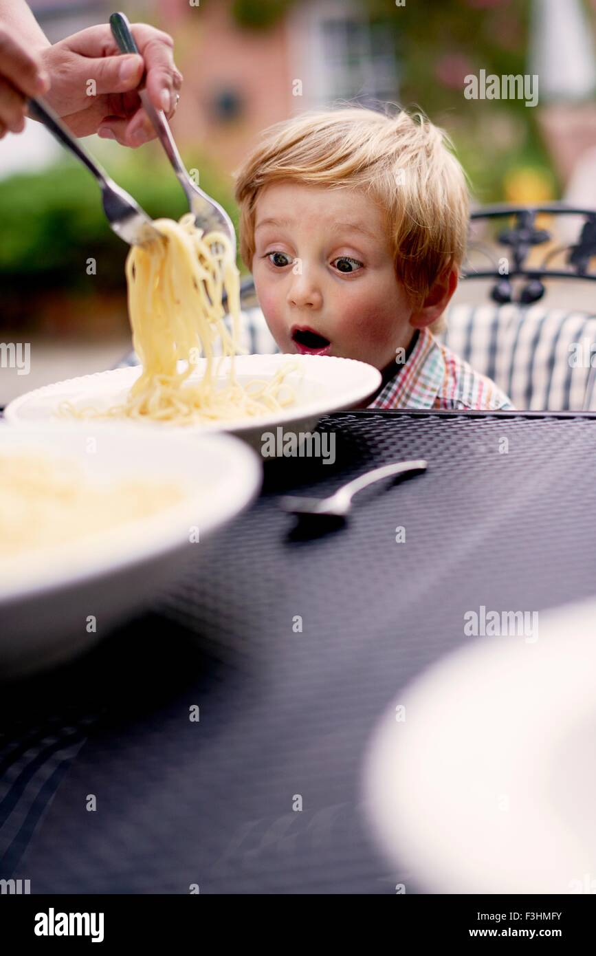 Muchacho sentado en la mesa de jardín que sirve los espaguetis, mirando sorprendido Foto de stock