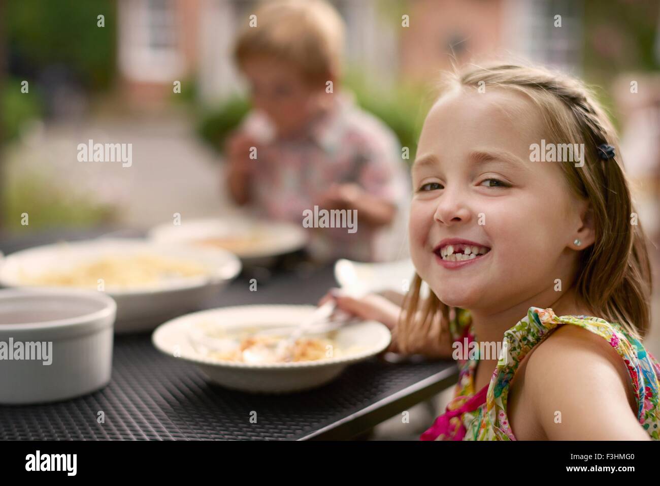 Chica comer en mesa de jardín, mirando por encima del hombro a la cámara sonrientes Foto de stock