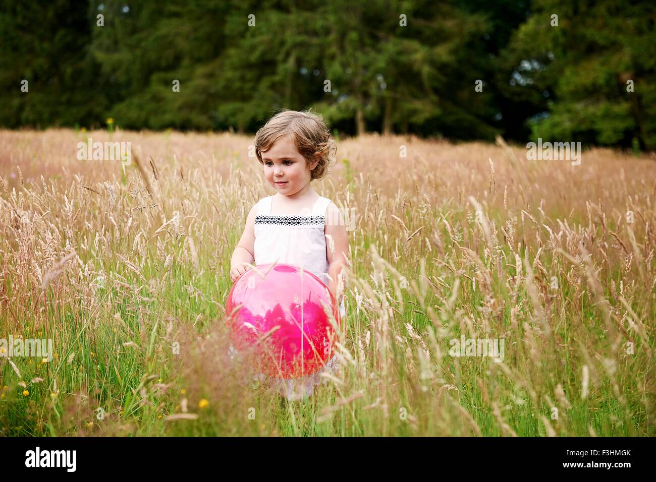Chica en el pasto alto sosteniendo globo rojo mirando lejos Foto de stock