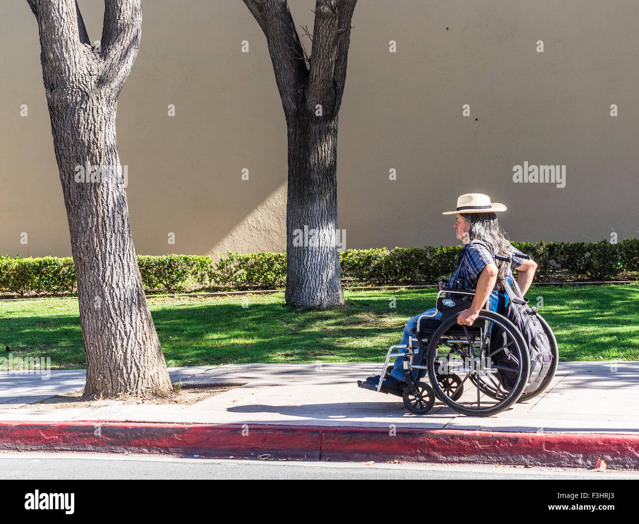 Discapacitados Una persona adulta de mediana edad se desplaza a lo largo de una acera en su silla de ruedas en un día soleado en Santa Barbara, California, USA. Foto de stock