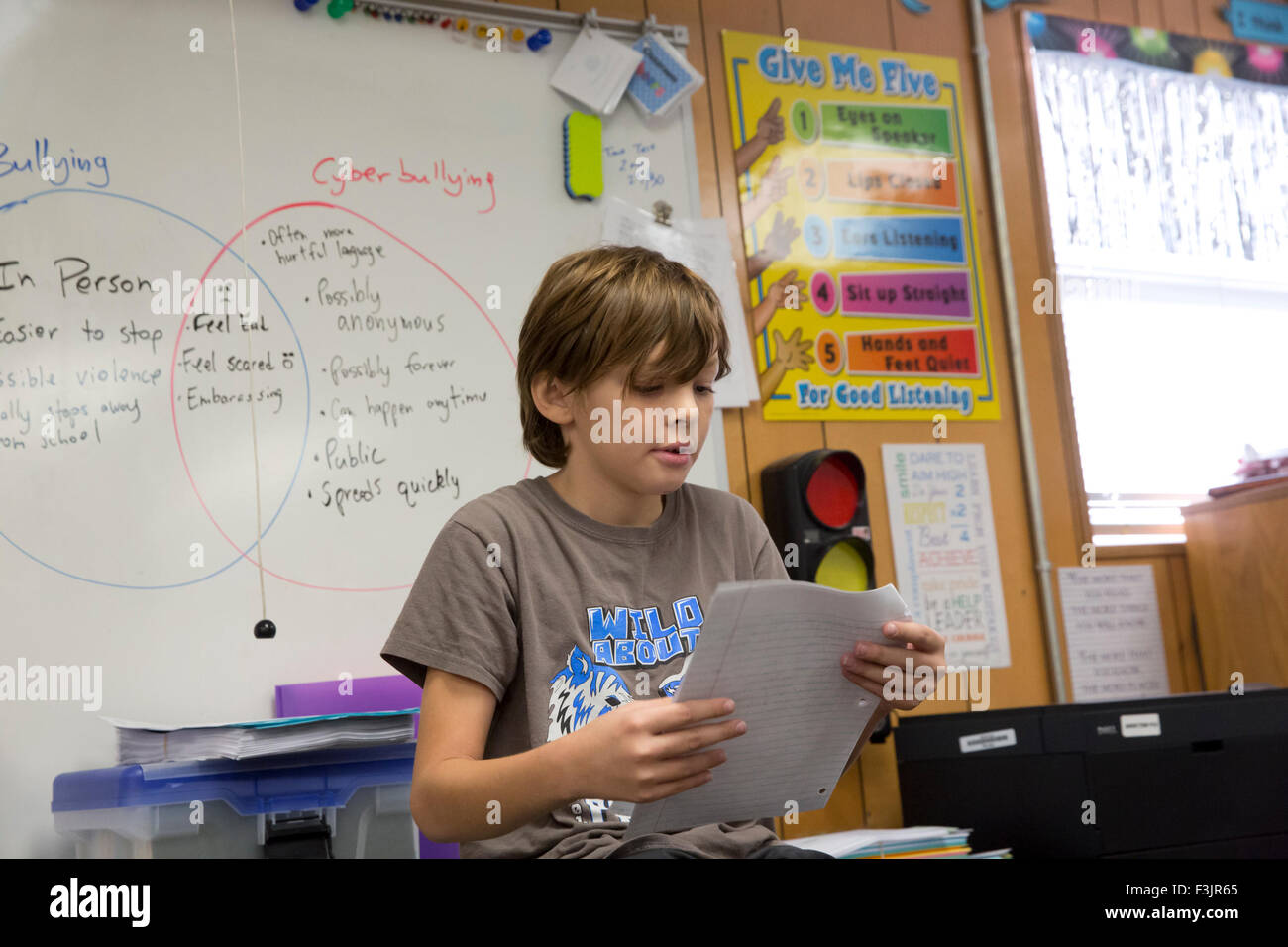 4º grado estudiante de primaria, un niño mexicano-americano de 10 años de edad lee un informe dentro de su aula Foto de stock