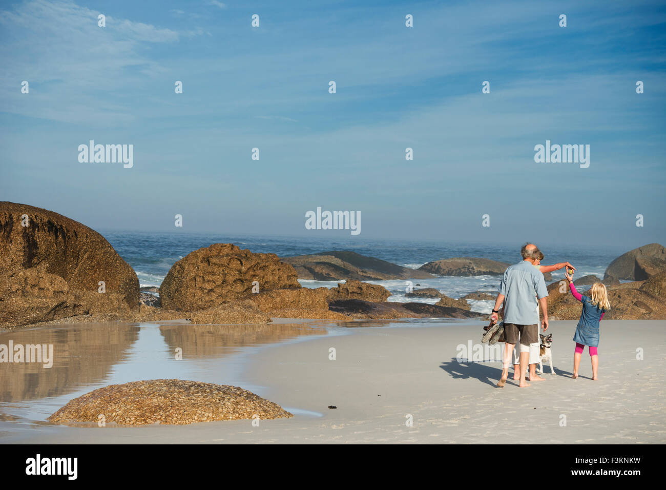 Familia en la playa de la Bahía del campamento al amanecer, Océano Atlántico, olas rompiendo en rocas de granito, Cape Town, Sudáfrica Foto de stock