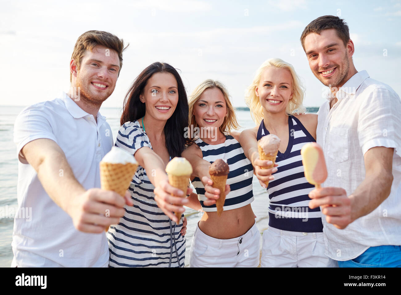 Sonriendo amigos comer helado en la playa Fotografía de ...