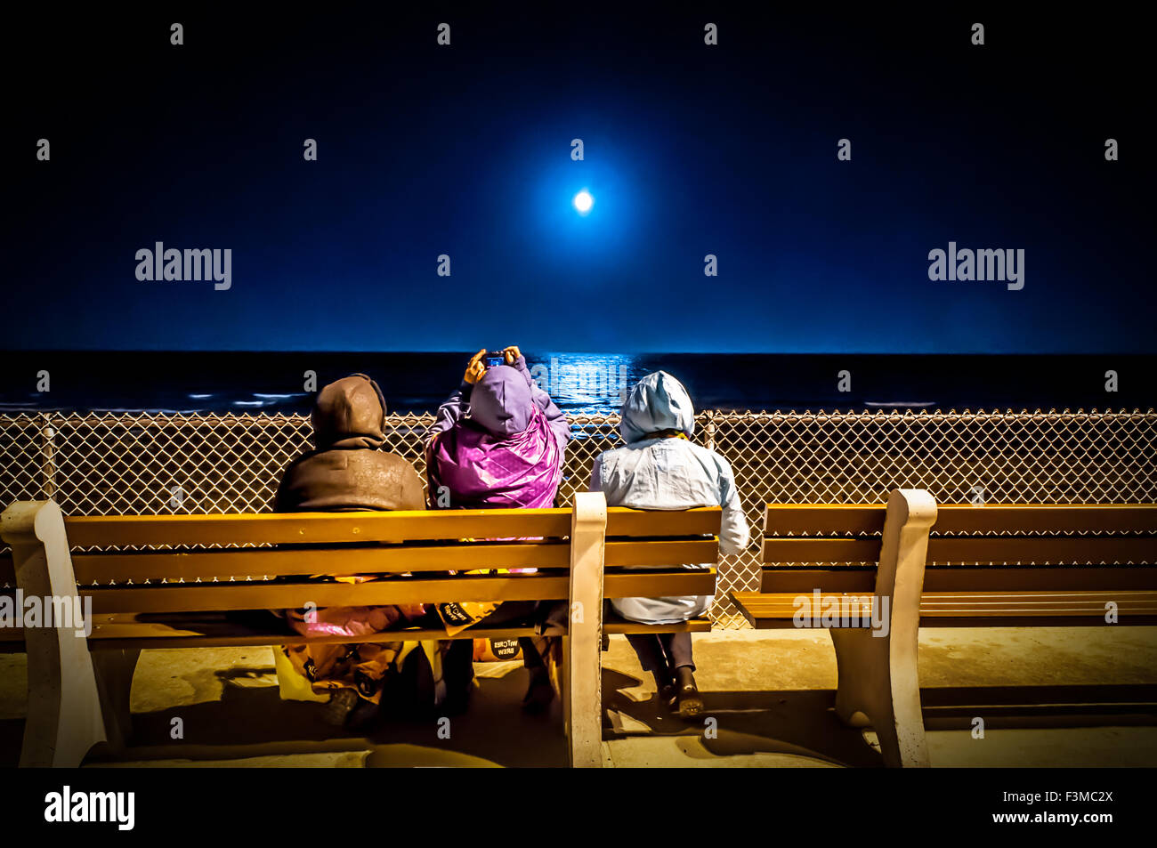 Tres señoras sentarse en un banco en el Ocean fotografiar, y ver la luna y  los anillos alrededor de ella, y una muy buena noche Fotografía de stock -  Alamy