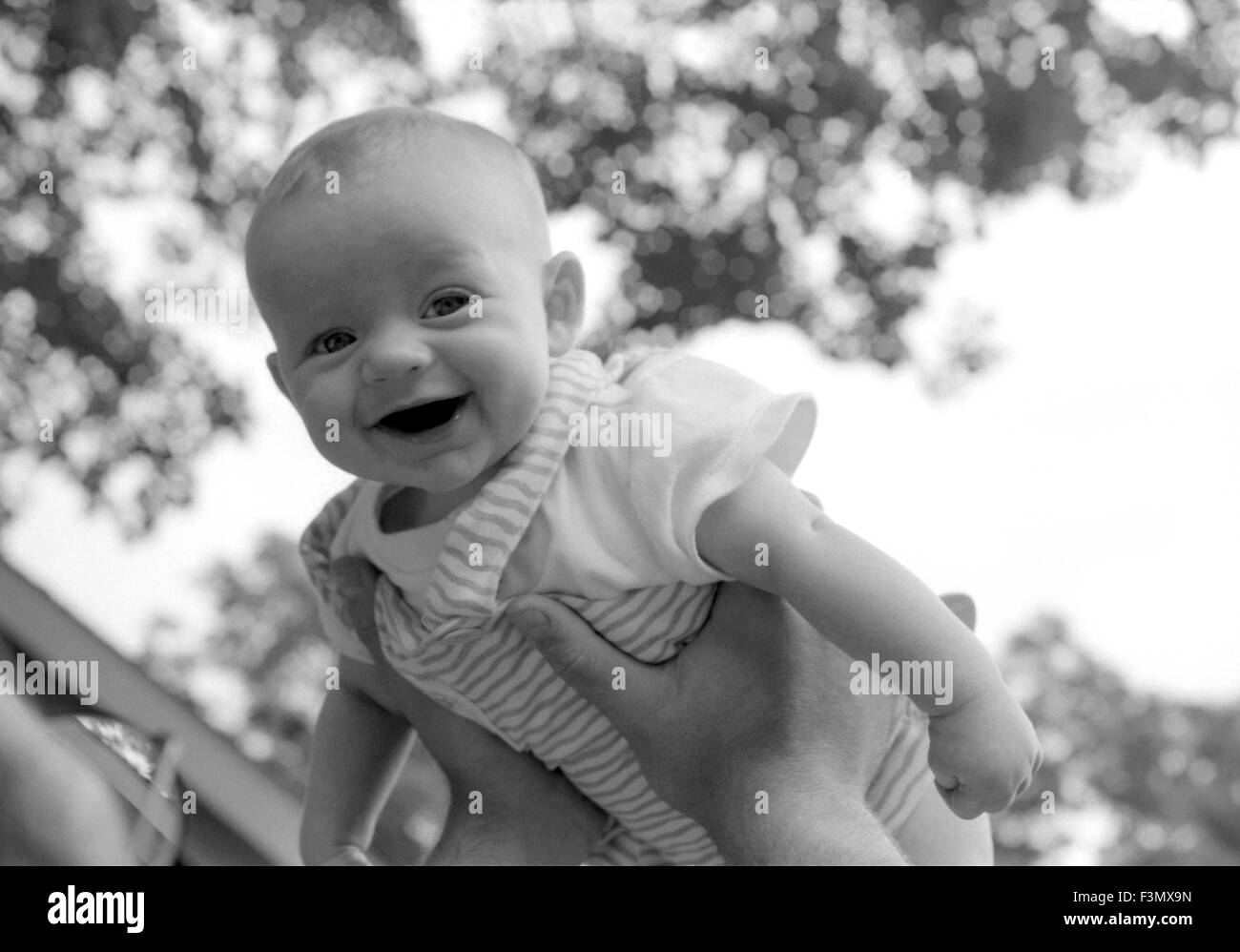 Bebé sonriente celebrada en el aire. Foto de stock
