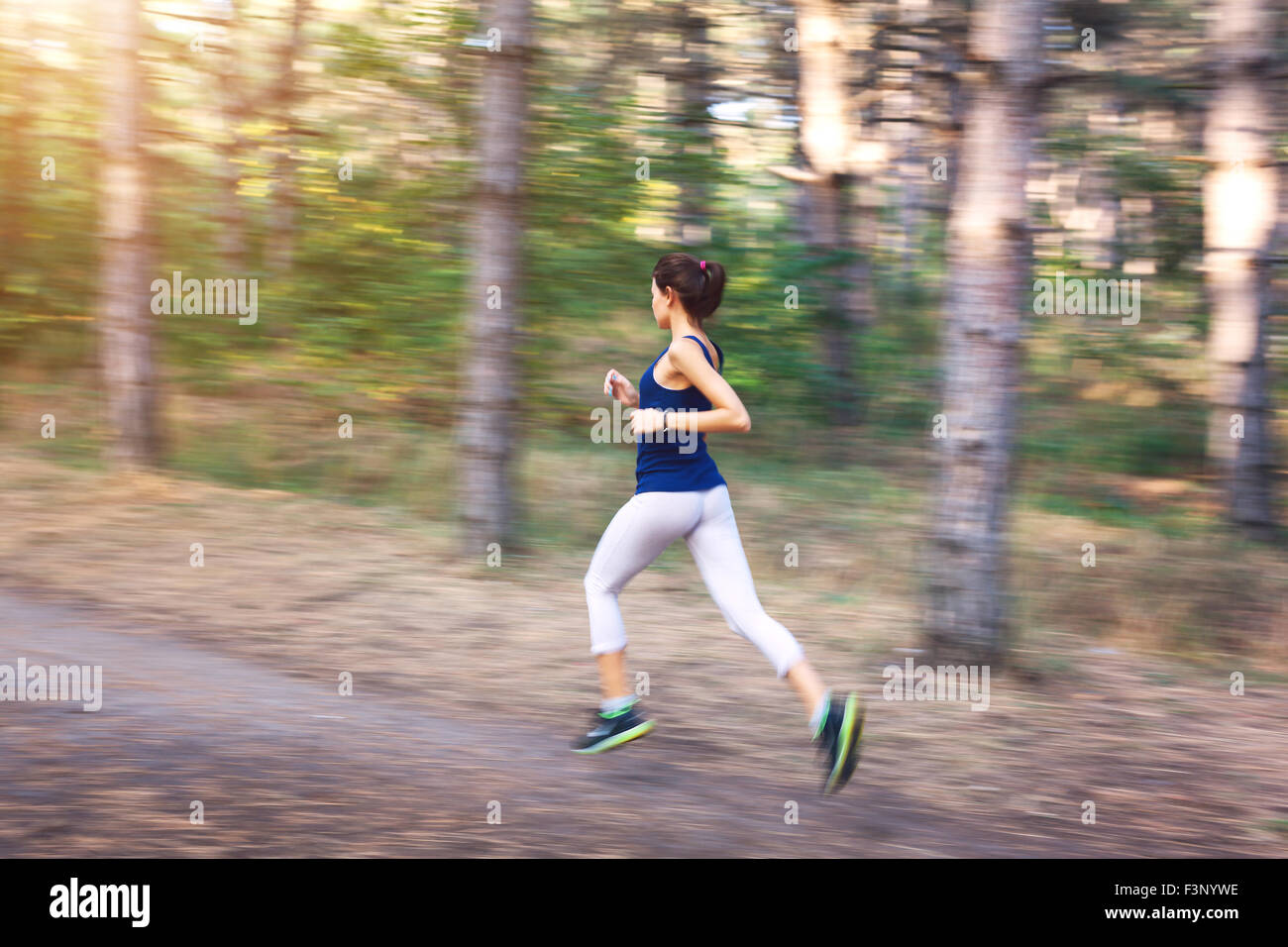 Mujer joven corriendo en un camino rural al atardecer en otoño del bosque. Antecedentes deportivos en el estilo de vida Foto de stock