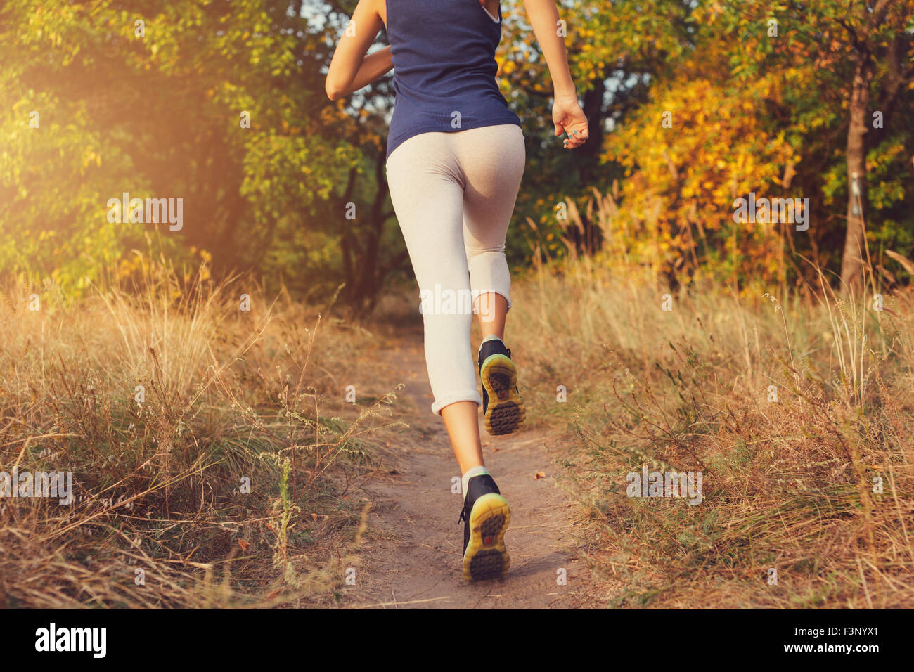 Mujer joven corriendo en un camino rural al atardecer en otoño del bosque. Antecedentes deportivos en el estilo de vida Foto de stock
