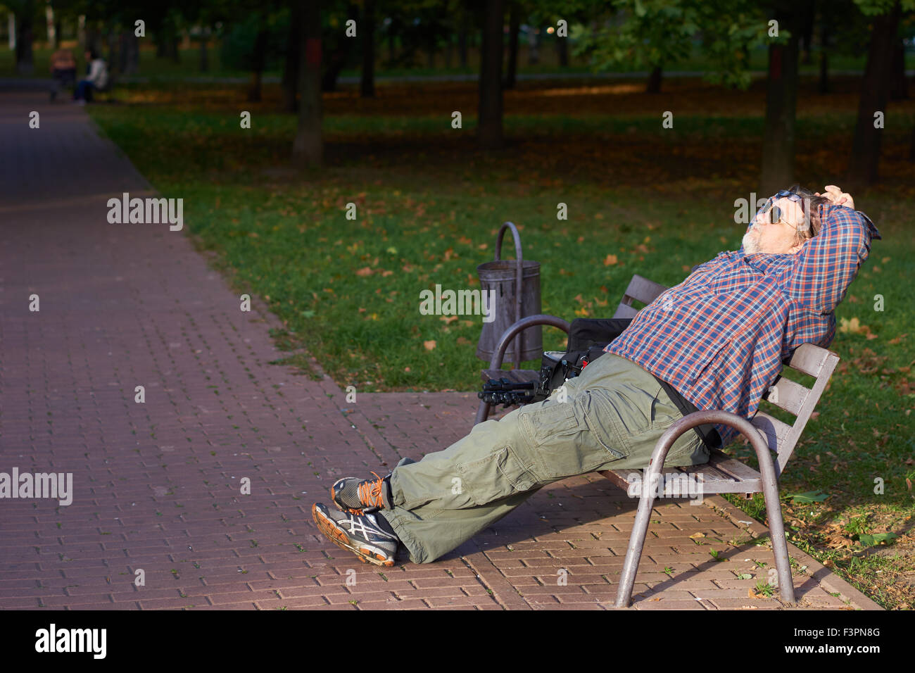 El hombre tiene el descanso en el parque de otoño bajo el sol Foto de stock