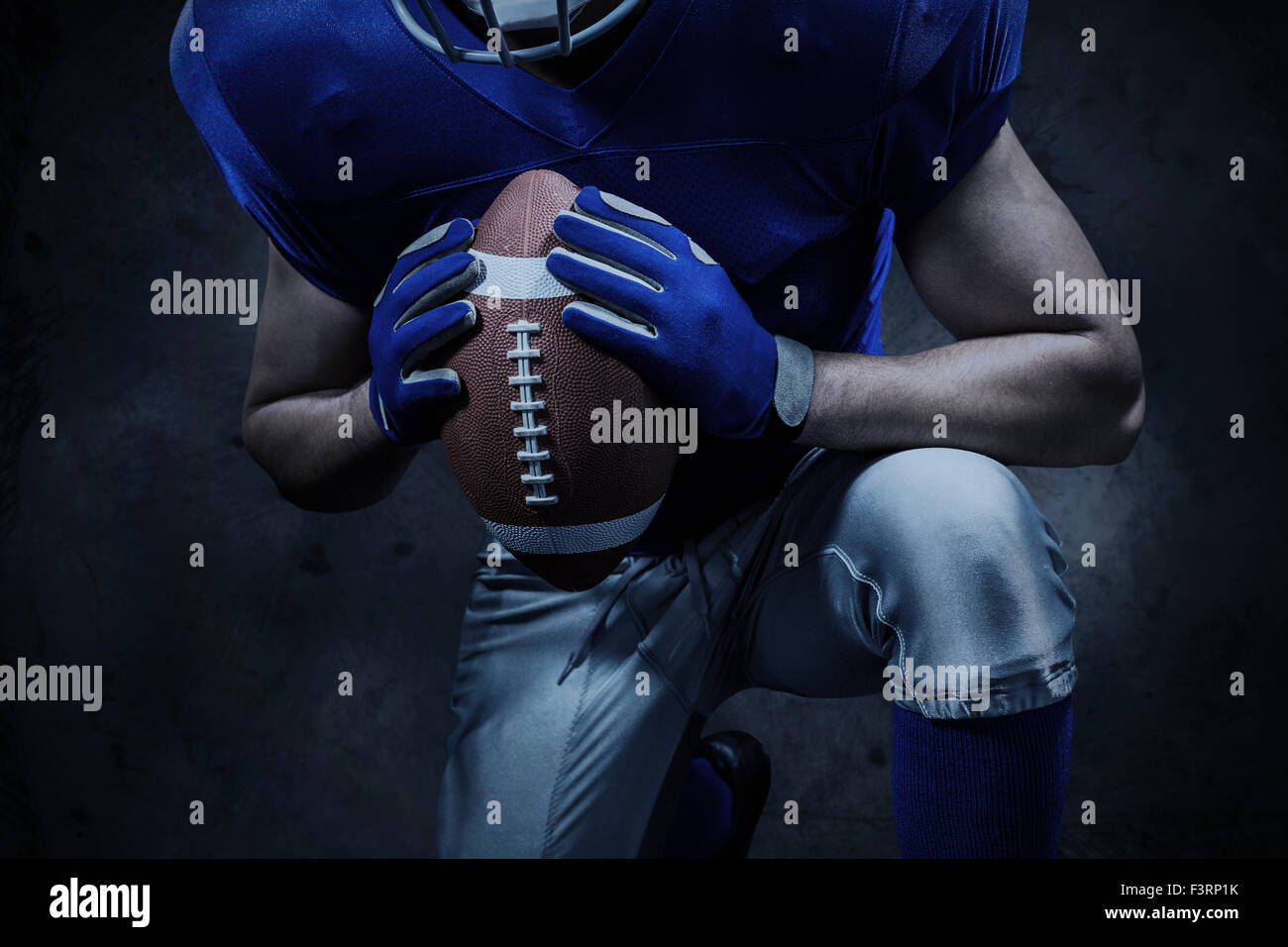 Imagen compuesta de la sección intermedia de jugador de fútbol americano de rodillas sujetando la bola Foto de stock