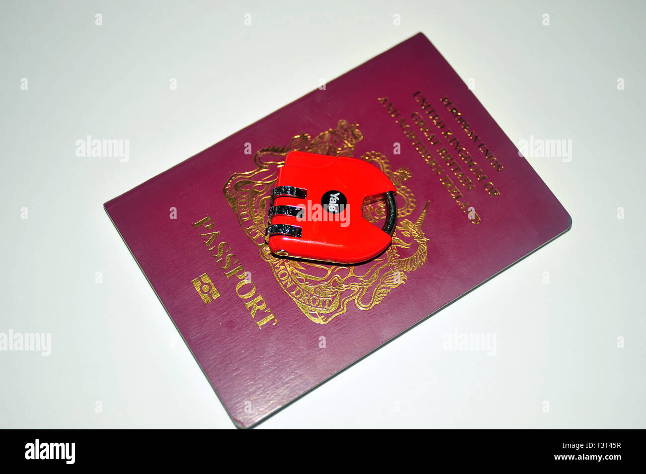 Un pasaporte británico rojo con una cerradura de combinación candado en la parte superior de éste. Foto de stock