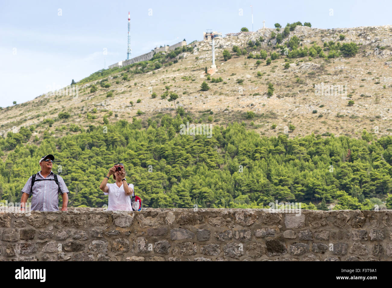 Dos turistas a las murallas de la ciudad de Dubrovnik, en Croacia. Monte Srd en el fondo. Foto de stock