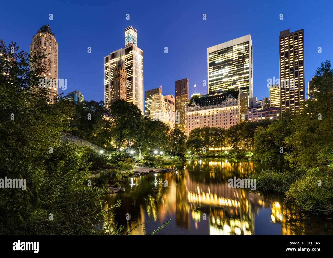 Los rascacielos de Manhattan iluminado la luz en las primeras horas de la noche. Los edificios reflejan el estanque en el Parque Central. La Ciudad de Nueva York. Foto de stock
