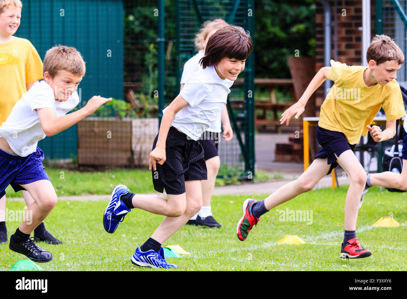 Inglaterra, escolares, niños, 10-11 años, corriendo la carrera sobre pista de césped al aire libre. En pantalones cortos y camiseta, mitad vista lateral de tres muchachos en ejecución. Foto de stock