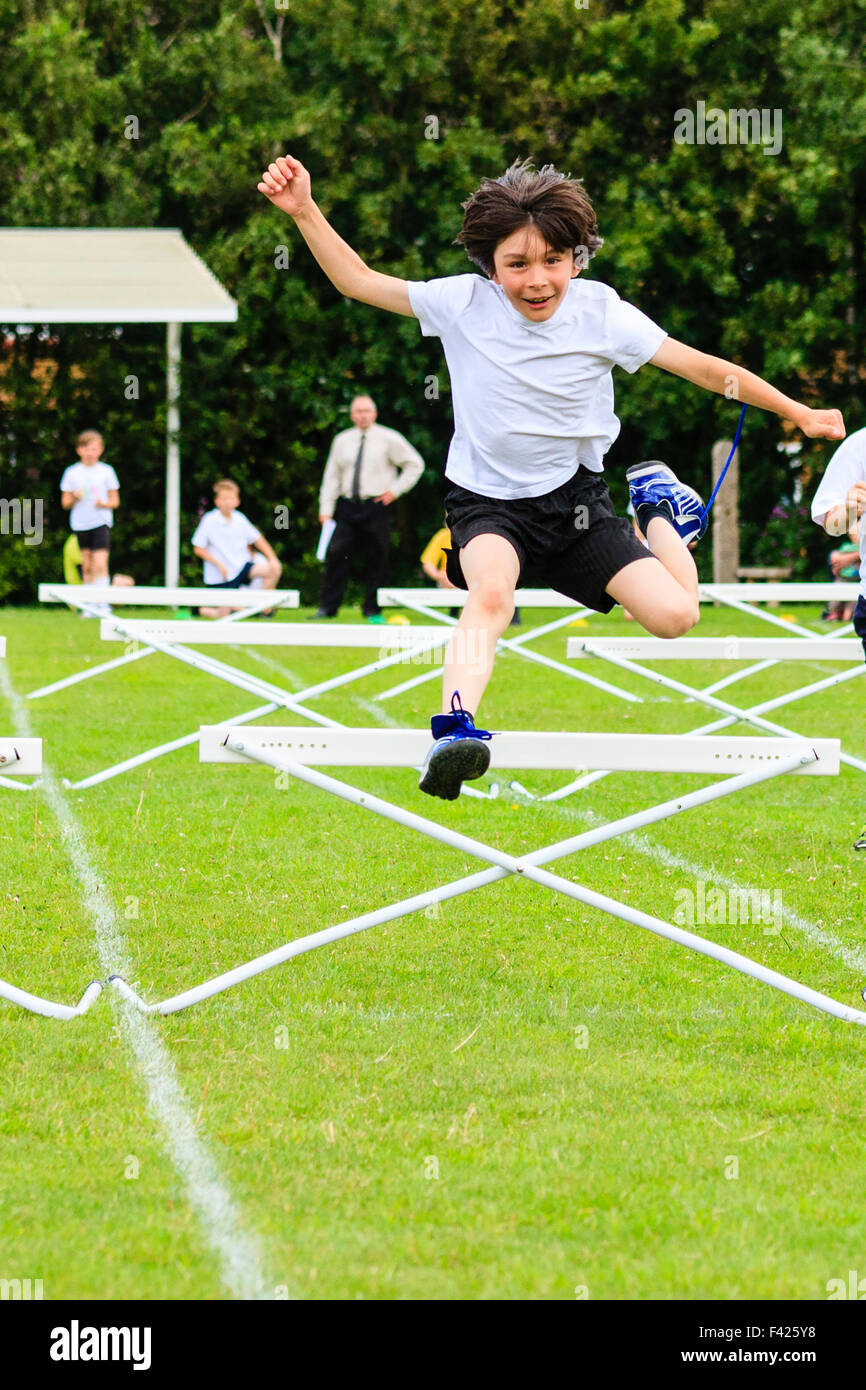 Día de Deportes de la escuela inglesa. Niño, joven, 10-11 años, saltan por  encima de obstáculos durante la carrera, el campo de deportes al aire  libre, carreras hacia el espectador Fotografía de