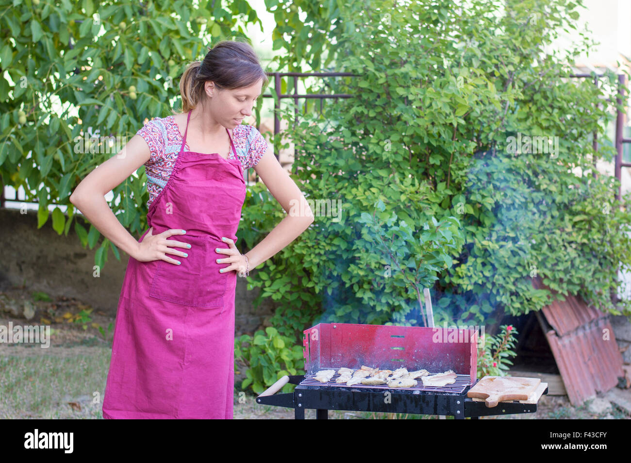 Apuesto joven mujer preparando la barbacoa en el patio Foto de stock