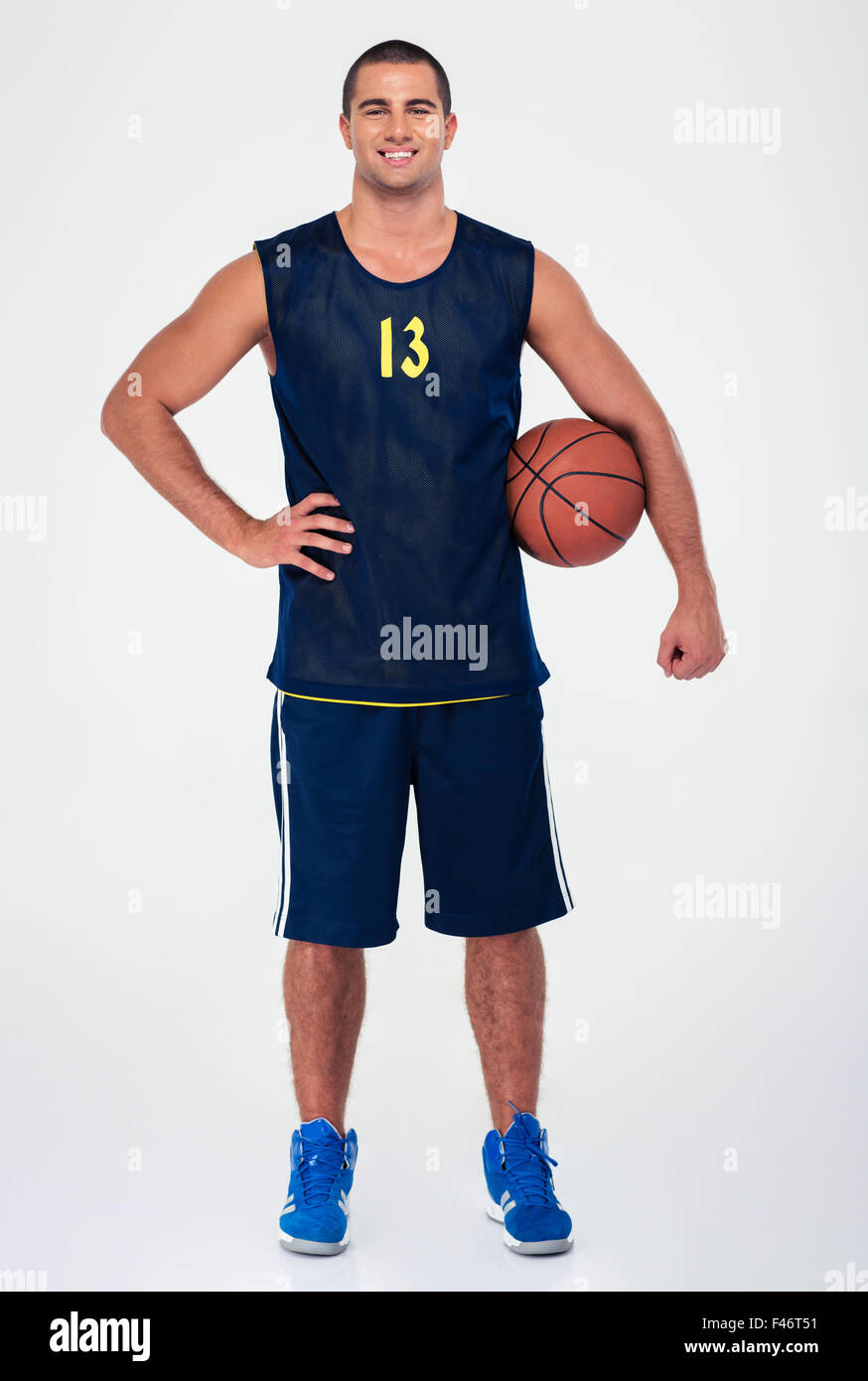 Retrato de longitud completa de un guapo jugador de baloncesto que se encuentran aisladas en un fondo blanco y mirando a la cámara Foto de stock