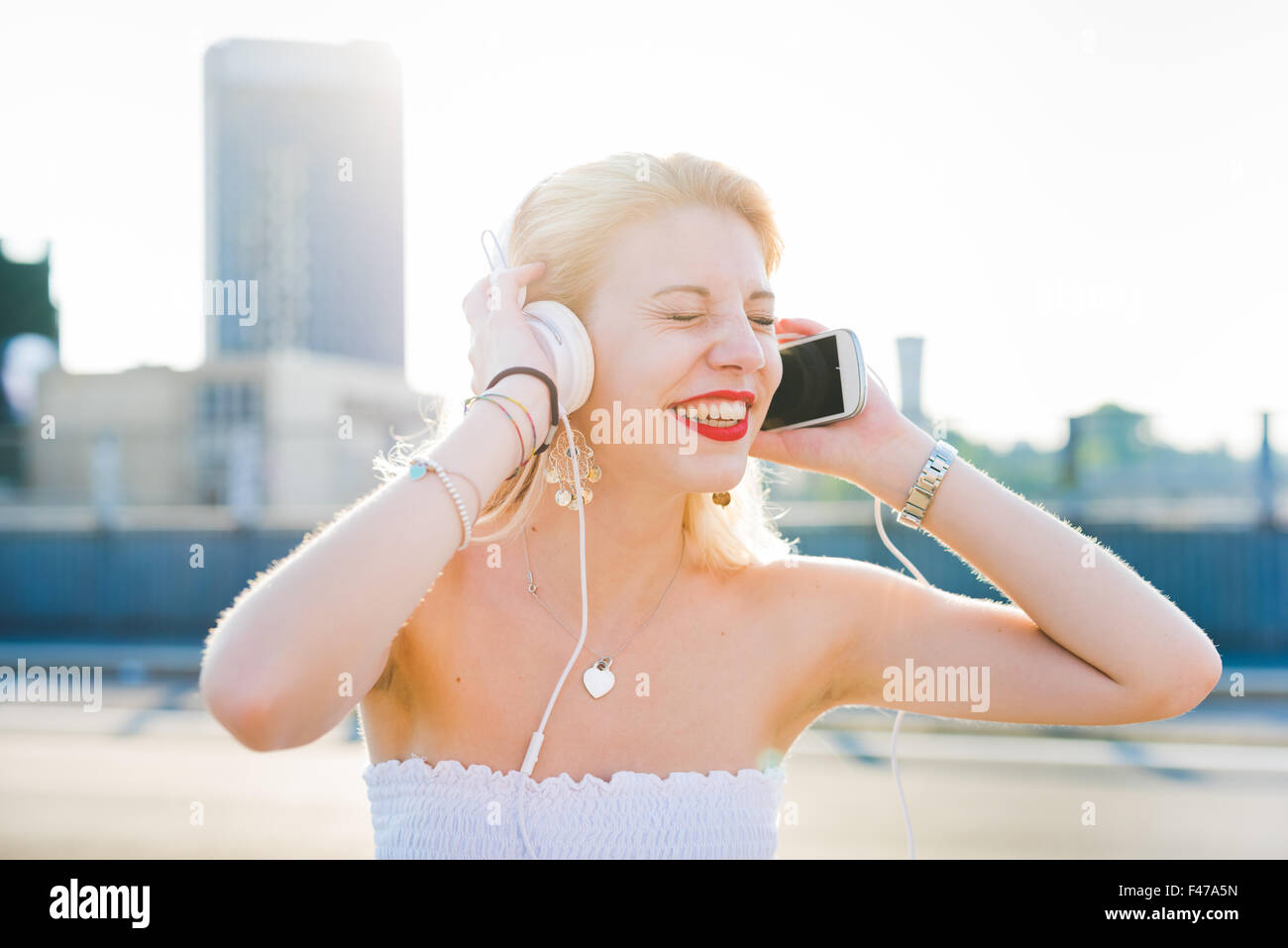 Longitud media retrato de joven apuesto caucásica rubia largo pelo recto mujer escuchando música con auriculares y smartphone Foto de stock