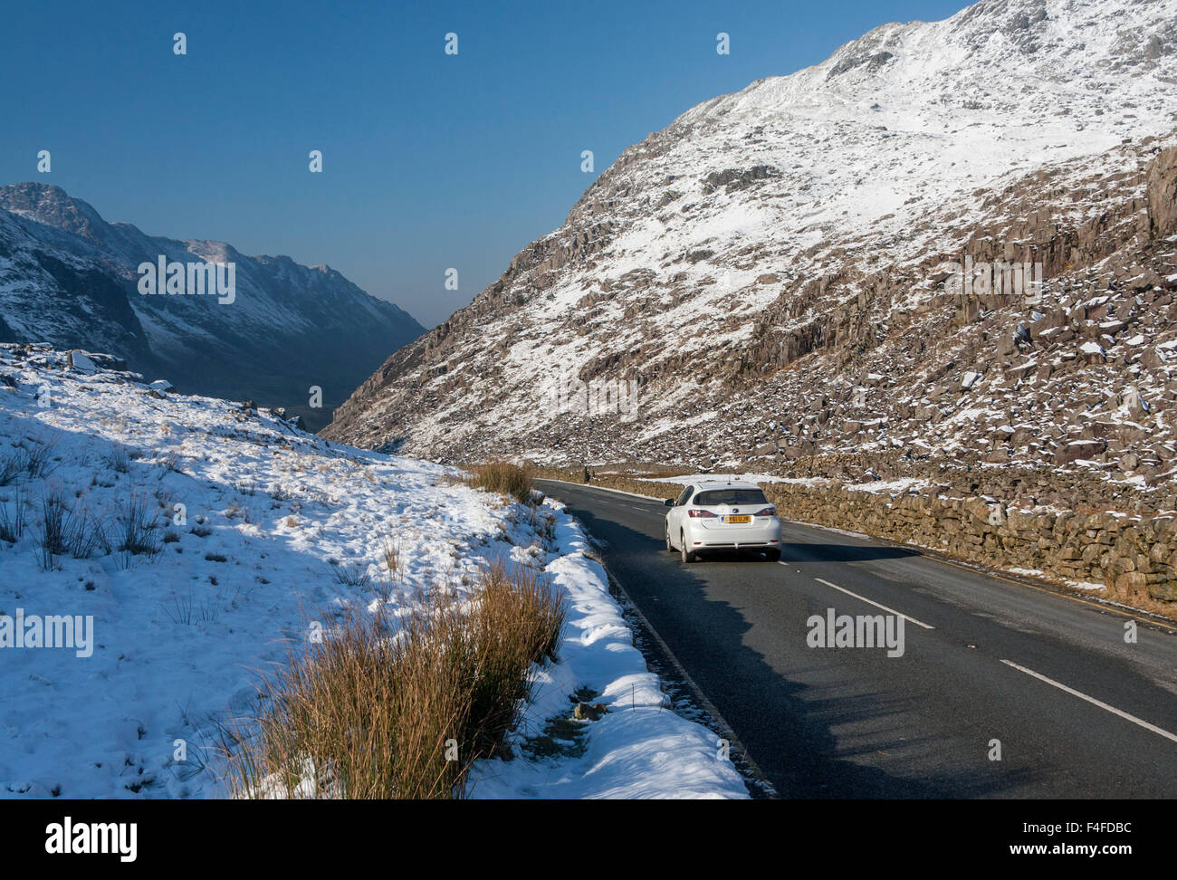 Llanberis Pass UN4086 road con coche pasando por disparo en invierno con nieve en las montañas Snowdonia NP Gwynedd North Wales UK Foto de stock