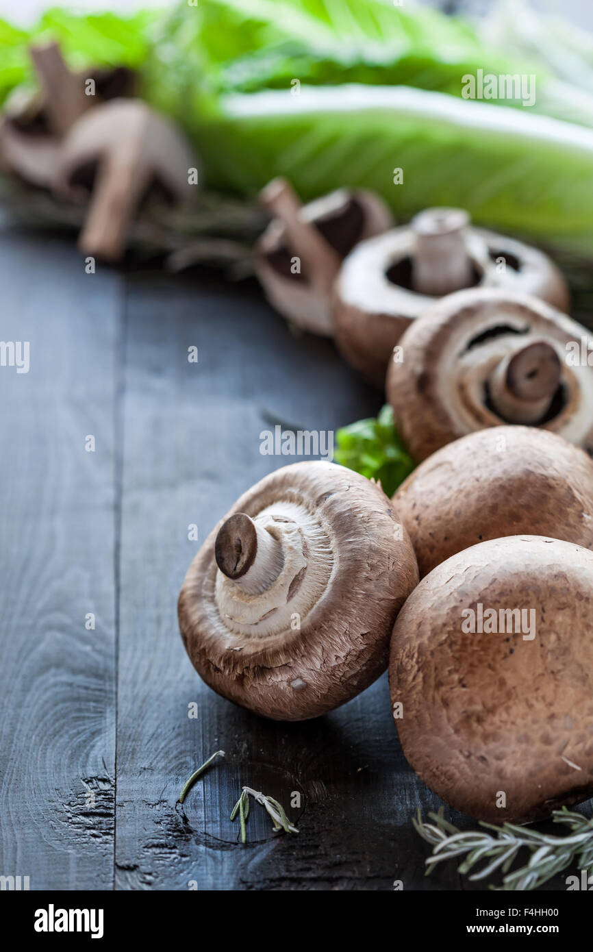 Hongos portobello fresca cruda con romero y ensalada de lechuga sobre fondo de madera Fotografía