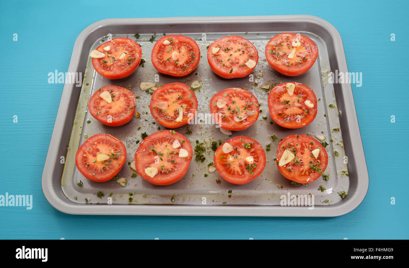 Los tomates en una bandeja para hornear, sazonado con tomillo y ajo, rociados con aceite de oliva para asar Foto de stock
