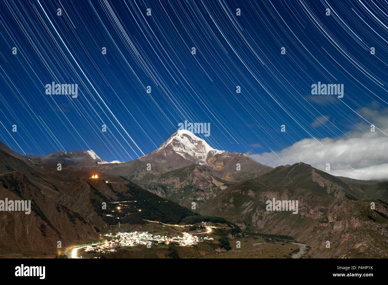 Moonlit vista de Estelas de estrellas sobre el Monte Kazbek (5047m), el pueblo de Gergeti Gergeti y Trinity Church, en el norte de Georgia. Foto de stock