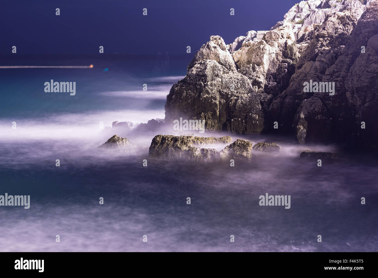 Las olas del mar línea de pestañas impacto rock en la playa de noche Foto de stock