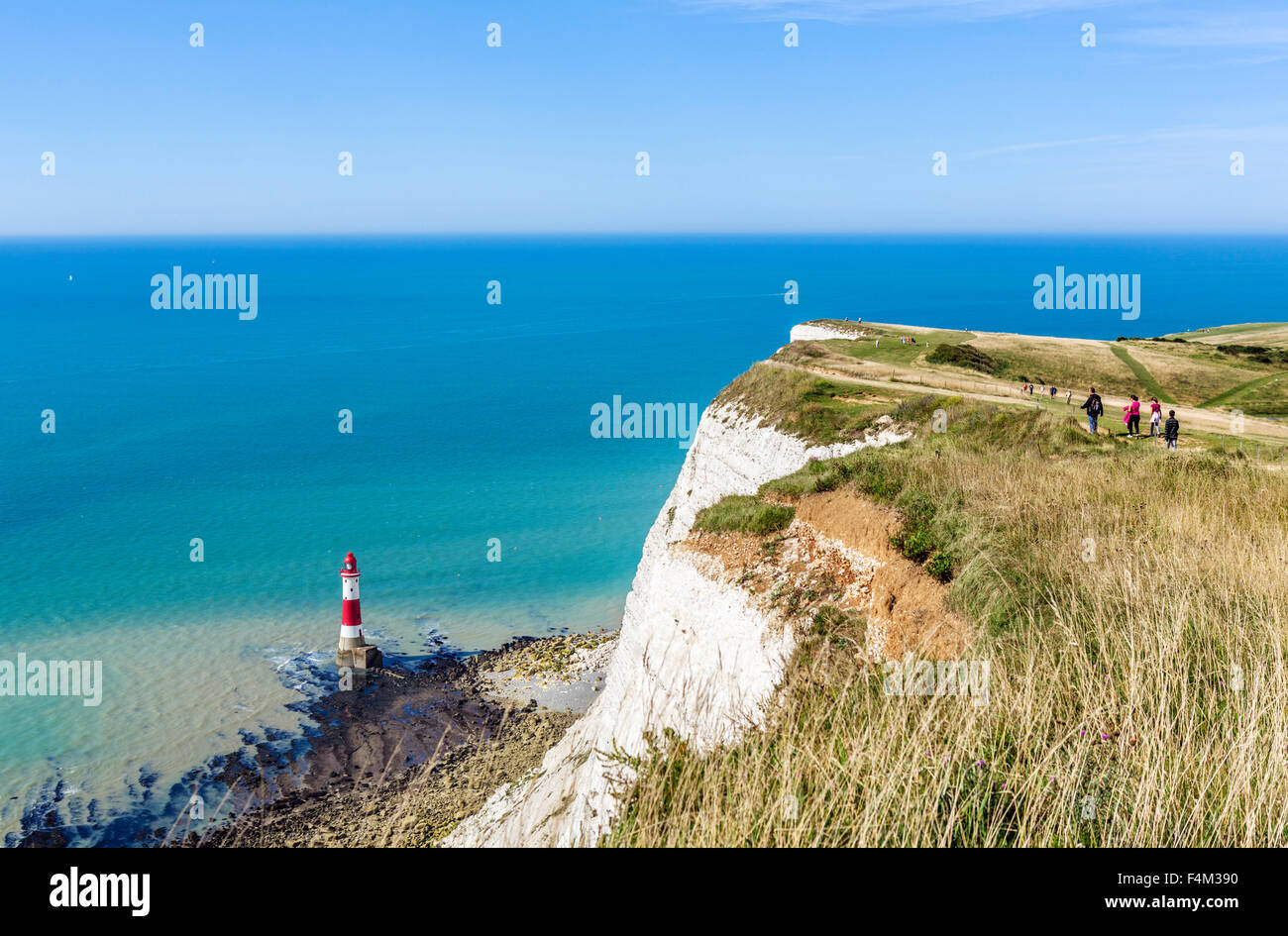 Los excursionistas en la ruta desde lo alto del acantilado con vistas al faro de Beachy Head, cerca de Eastbourne, East Sussex, Inglaterra, Reino Unido. Foto de stock