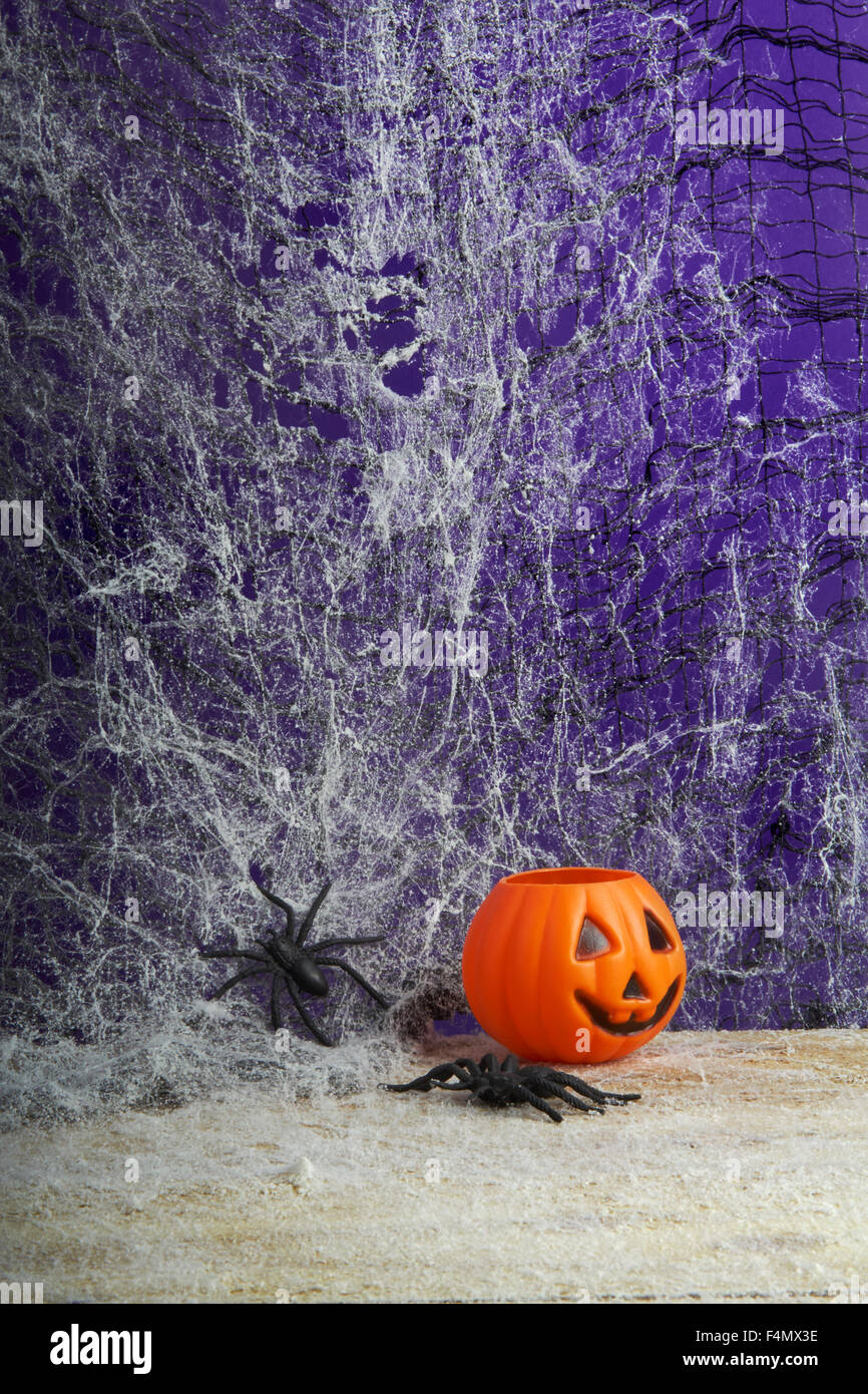 Concepto de Halloween con forma de calabaza naranja tealight portavelas de juguete y cruceta en una telaraña de fondo oscuro Foto de stock