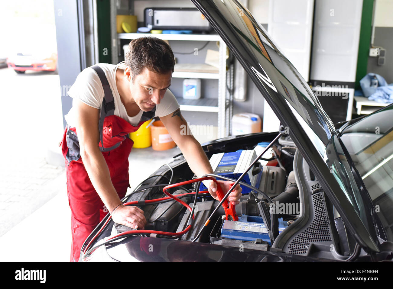 Mecánico de automóviles que trabajan en taller de reparaciones, recargar la batería del automóvil Foto de stock