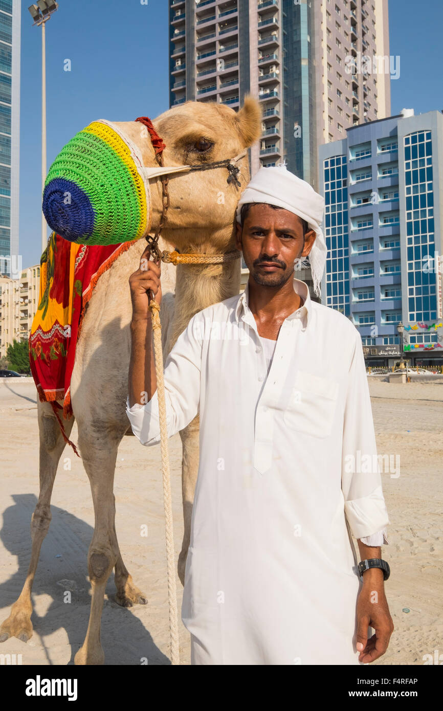Hombre con camel caminando por la playa en la costa del emirato de Ajman, en los Emiratos Árabes Unidos Foto de stock
