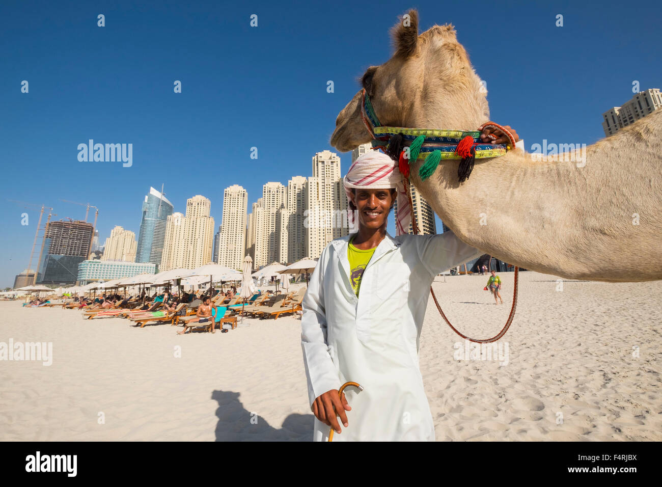 Turismo y propietario de camello en la playa en JBR residencias de Jumeirah Beach en la zona del puerto deportivo de Dubai, Emiratos Árabes Unidos Foto de stock