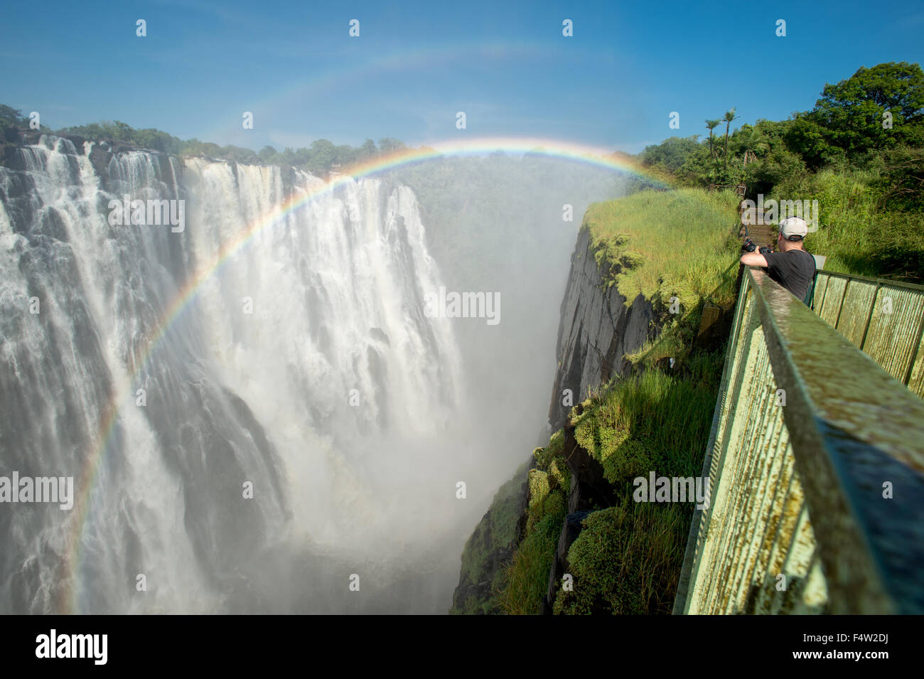 LIVINGSTONE, ZAMBIA - Turista con la cámara a través de las Cataratas Victoria cascada con rainbow Foto de stock