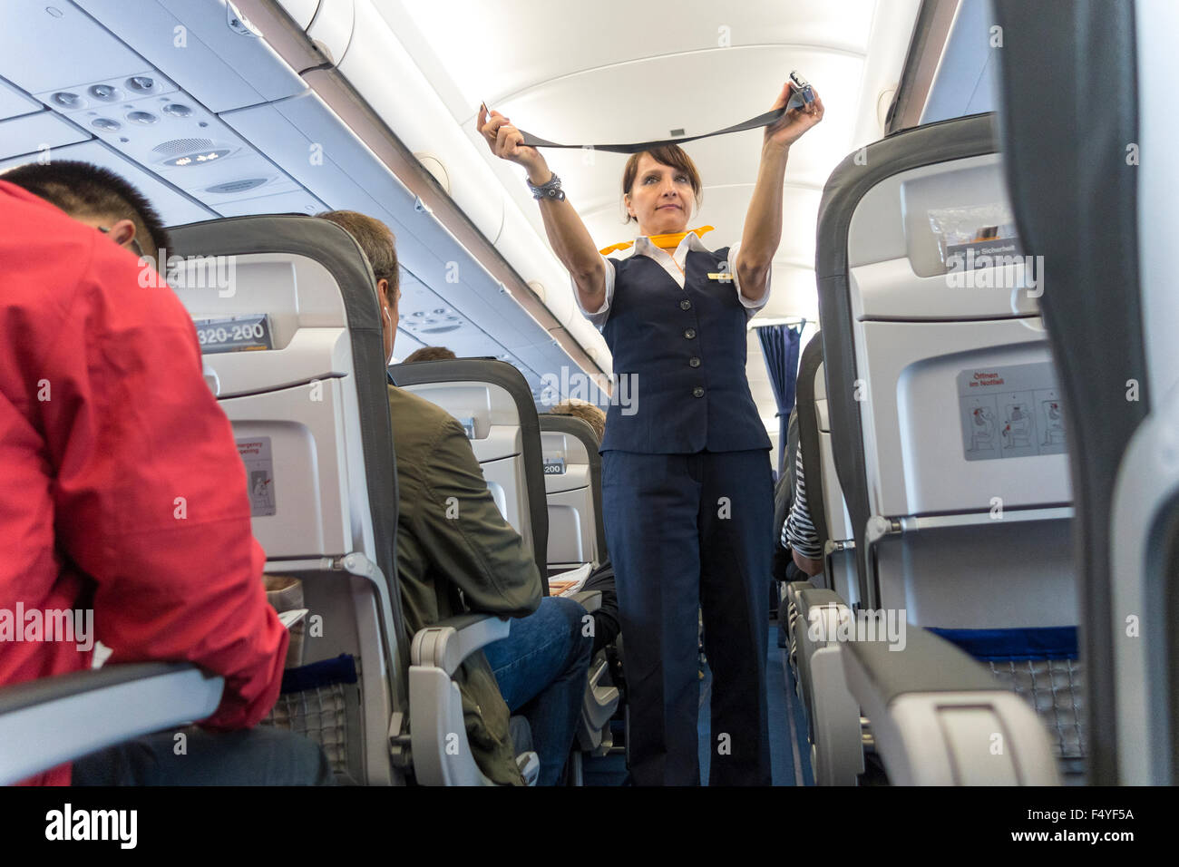 Azafata femenina demostrando el cinturón de seguridad en las instrucciones de seguridad en avión de Lufthansa Foto de stock