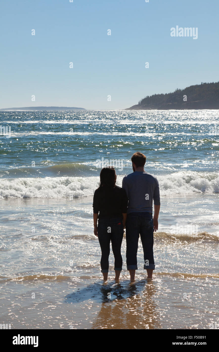 Una pareja de pie en el borde del agua mirando al mar, Maine, Estados Unidos. Sólo para uso editorial Foto de stock