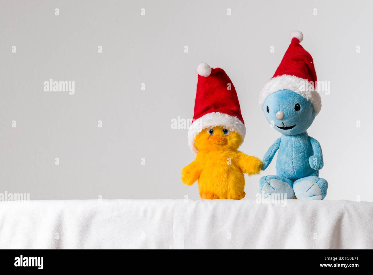 Una luz azul y amarillo de peluche, vistiendo gorros de Santa Claus, están sentados juntos en una mesa blanca Foto de stock