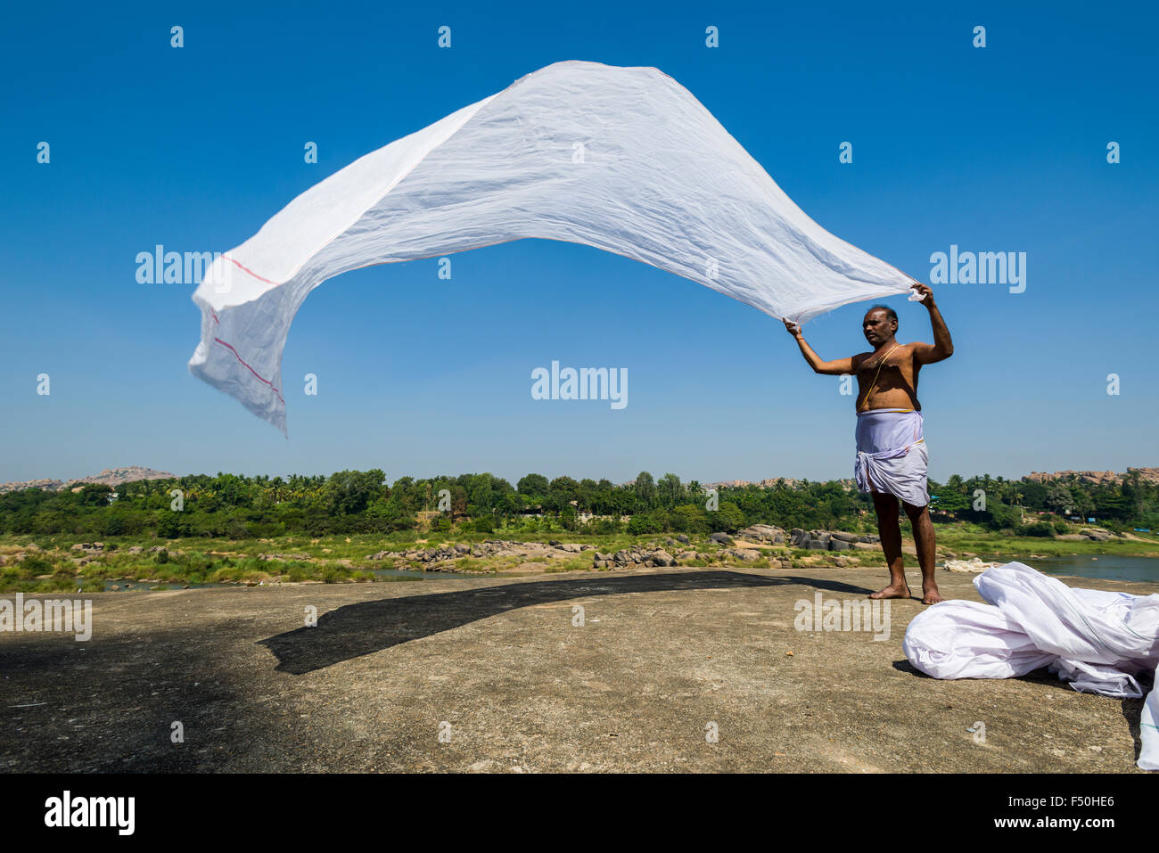 Un hombre, de pie sobre una roca, se está secando su blanca lunghi en el viento Foto de stock
