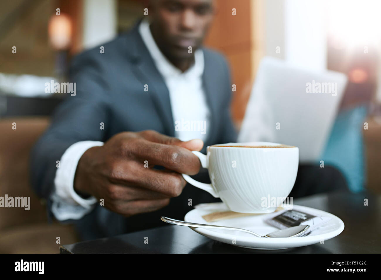 Primer plano de joven 's mano recogiendo una taza de café. Empresario sentado en el vestíbulo del hotel bebiendo café. Foto de stock