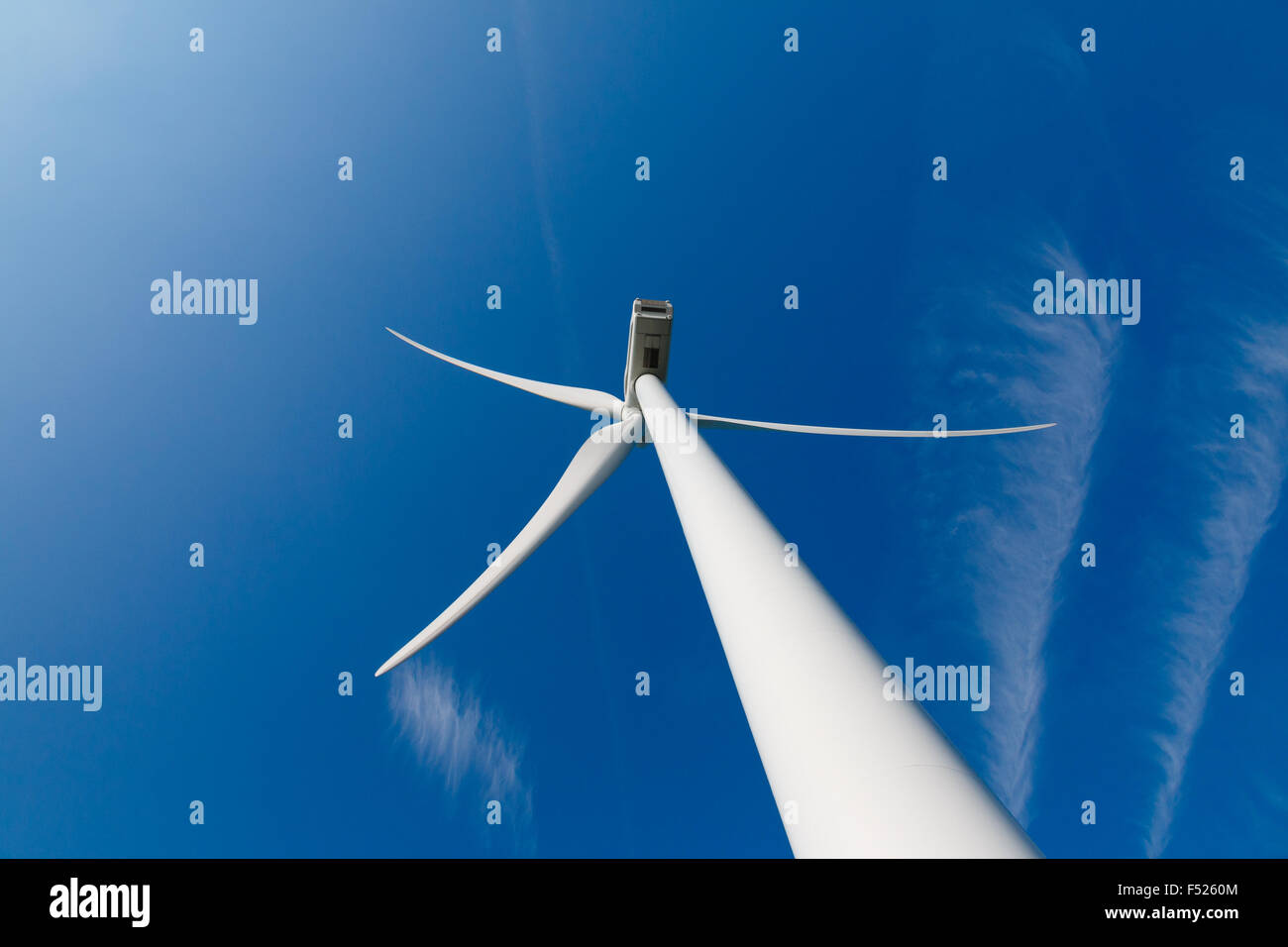 Turbina de viento arriba desde la parte trasera y las estelas de condensación de aviones en el cielo azul Foto de stock