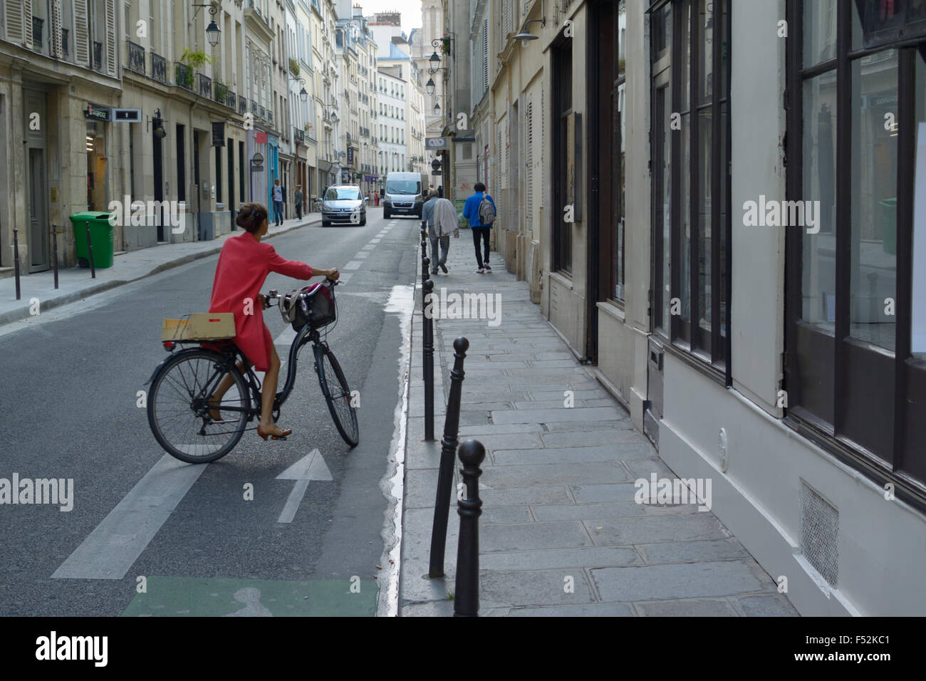 Mujer en rojo montando una bicicleta en el Marais de París, FR Foto de stock